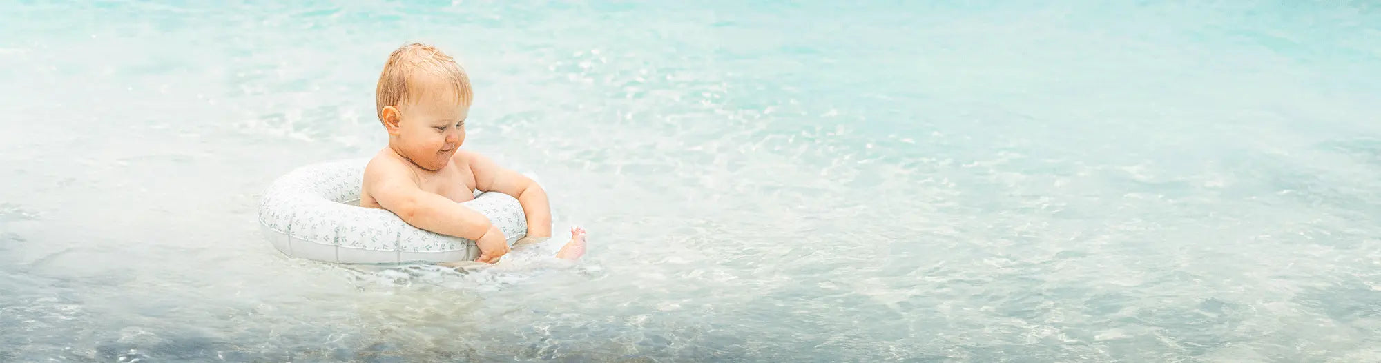 Baby in zwembandje speelt lachend in ondiep, helder zeewater.
